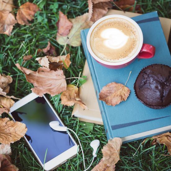 Bog der ligger i efterårsblade med kage og kaffe ovenpå