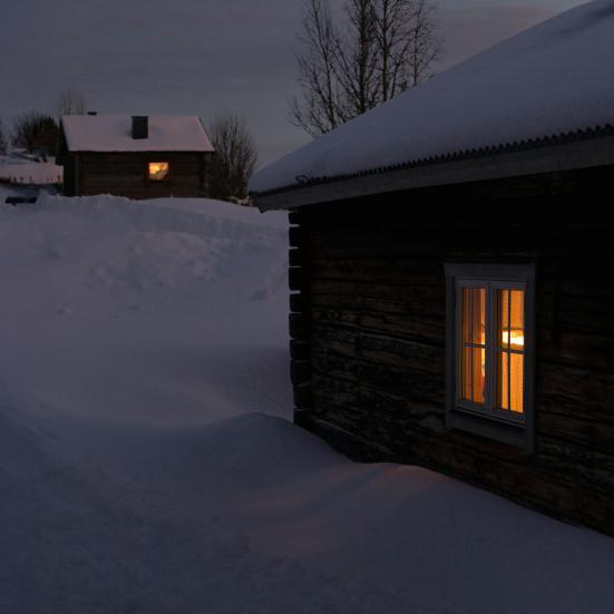 et hus står snedækket i mørket med varmt, gyldent lys i vinduerne