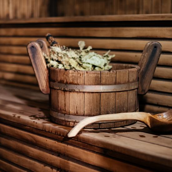 En sauna af træ indefra. Der står en træspand med urter på træbænken med en træske liggen foran