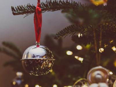 billedet viser en blankpoleret juleklokke i messing der hænger på en gren på et juletræ med lys og anden pynt