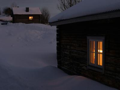 et hus står snedækket i mørket med varmt, gyldent lys i vinduerne